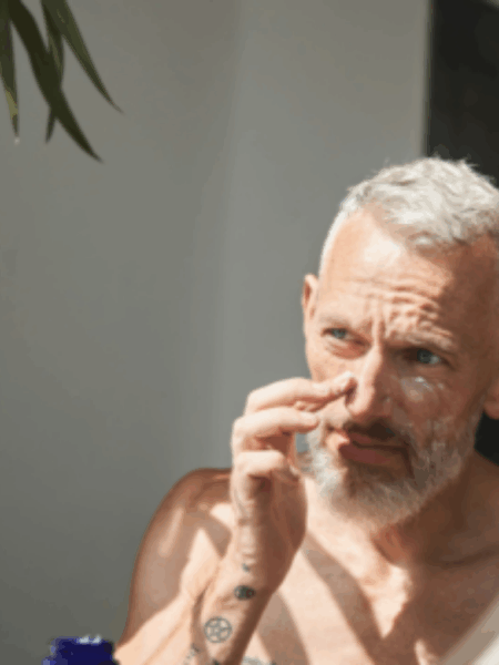 Man putting lotion onto his face looking in the mirror.