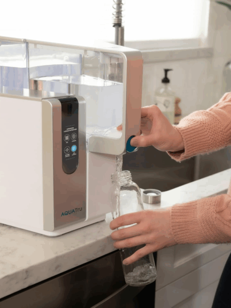 Women at the kitchen counter pouring water into a glass from a reverse osmosis countertop system.