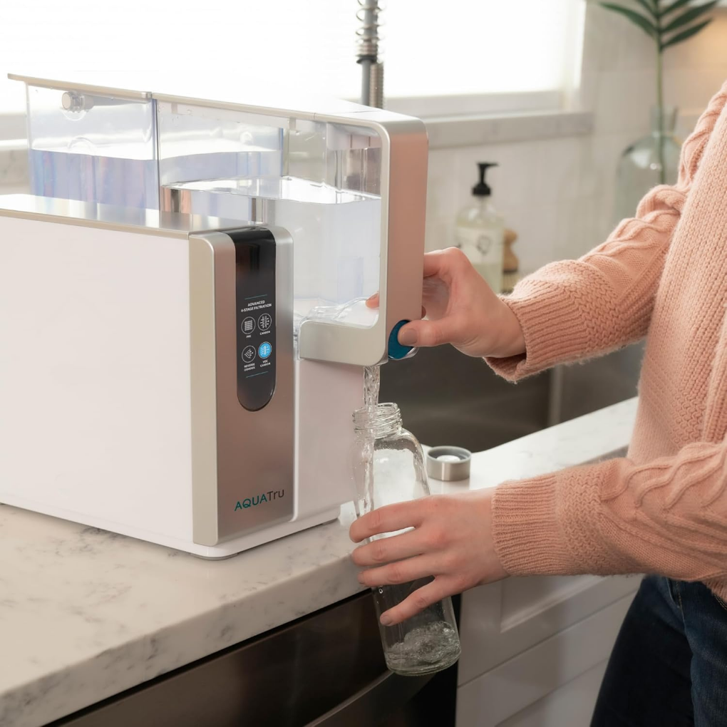 Women at the kitchen counter pouring water into a glass from a reverse osmosis countertop system.