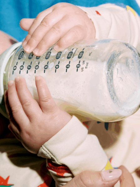 Baby drinking out of a glass baby bottle.