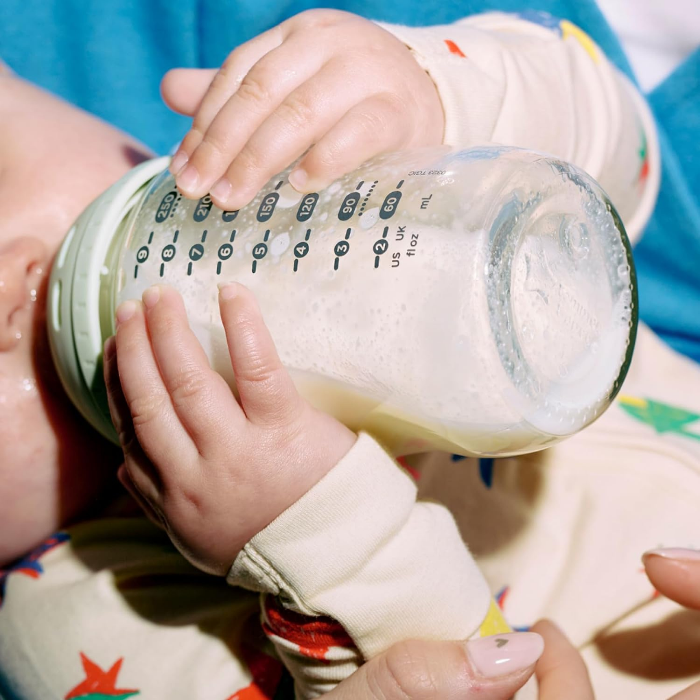 Baby drinking out of a glass baby bottle.