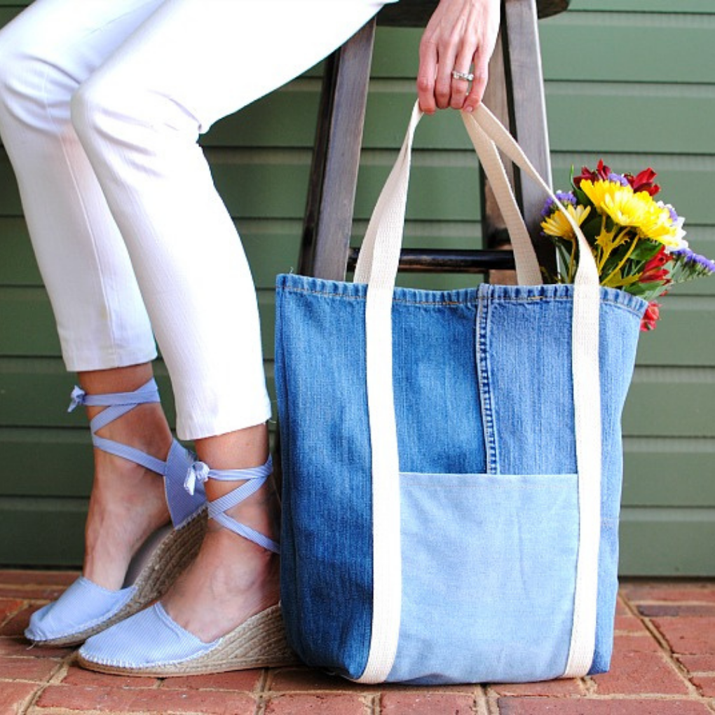 A woman sitting in a chair with her denim DIY bag next to hear with flowers popping out of the top of the bag.