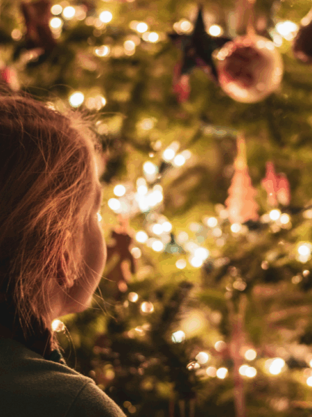 Young girl looking at a lit up Christmas tree.