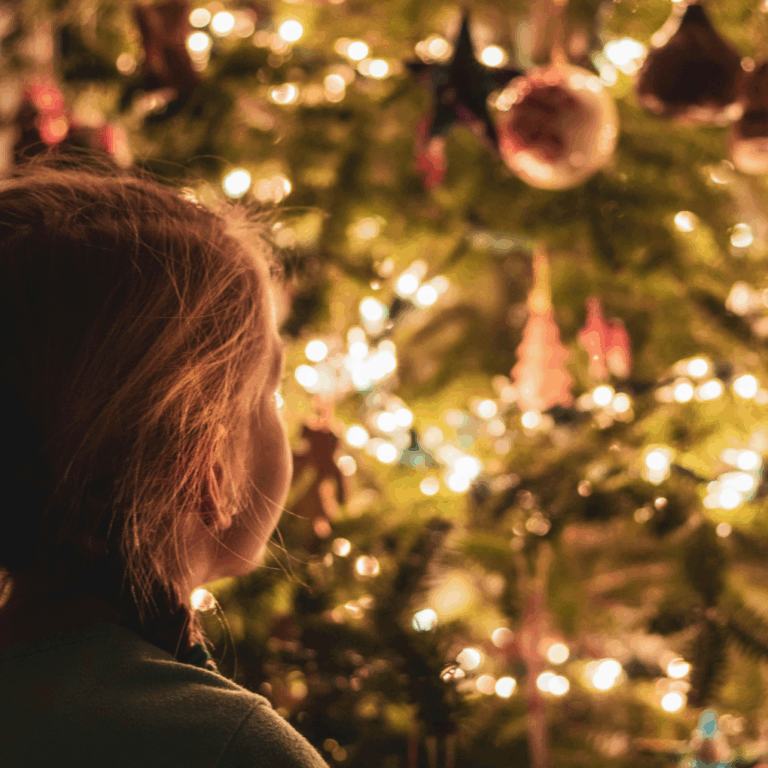 Young girl looking at a lit up Christmas tree.