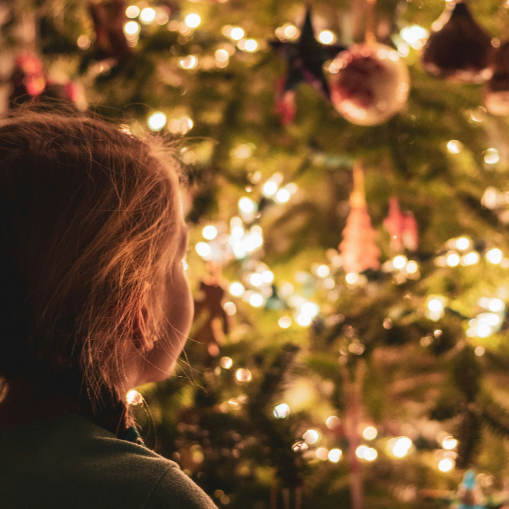 Young girl looking at a lit up Christmas tree.