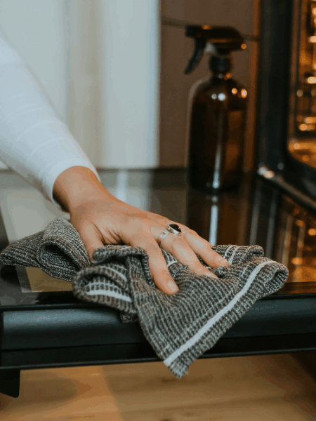 Person wiping down an open oven door with a cloth while using natural cleaning supplies.