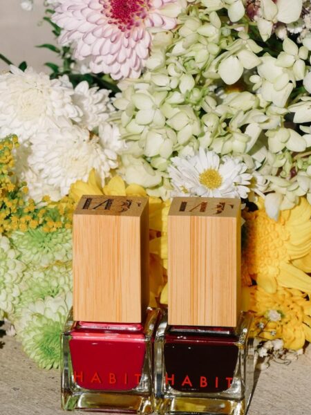 Non toxic nail polish Habit 2 bottles sitting next to each other in front of flowers