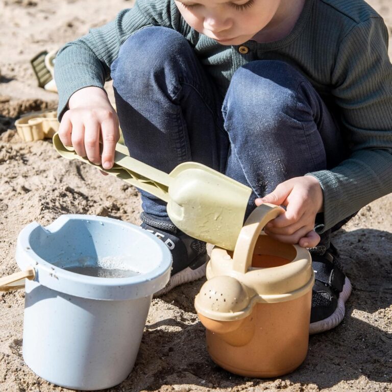 Boy on the beach filling up his beach toys with sand.