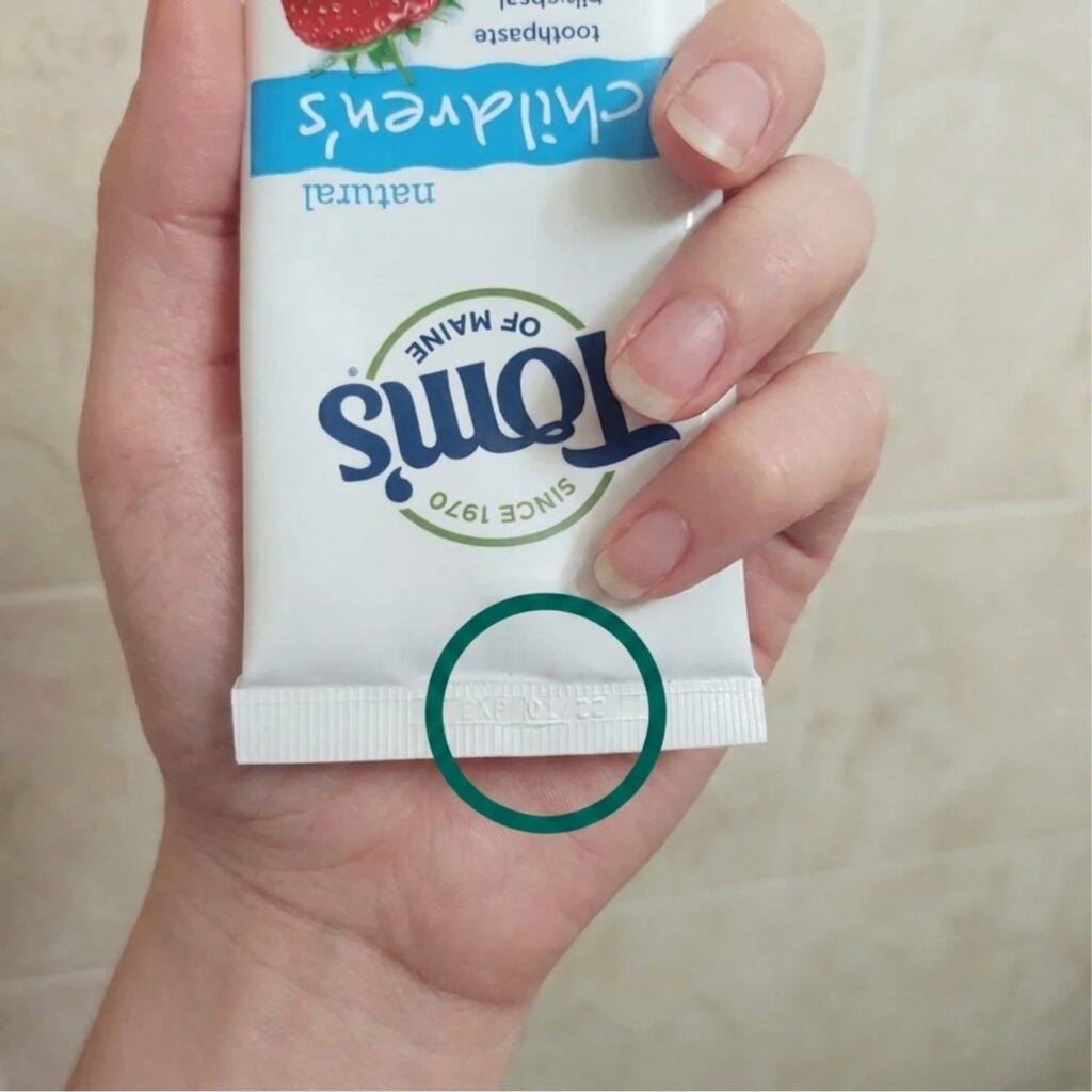 A woman holding a Tom's toothpaste in her hand, with the expiration date circled in green.