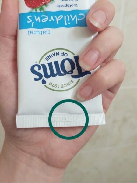 A woman holding a Tom's toothpaste in her hand, with the expiration date circled in green.