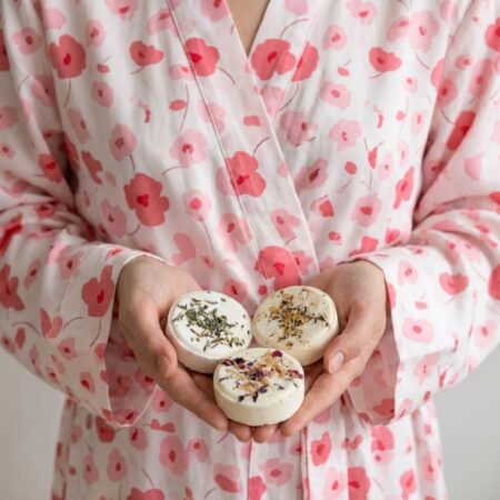 Woman in a pink floral robe holding three round shower steamers in her hands