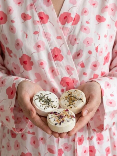 Woman in a pink floral robe holding three round shower steamers in her hands