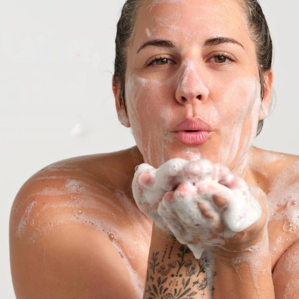 Woman soaping her face with Castile soap and blowing soap off her hands.