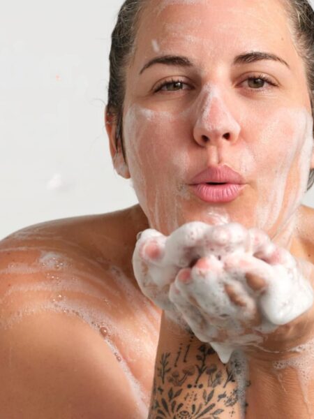 Woman soaping her face with Castile soap and blowing soap off her hands.