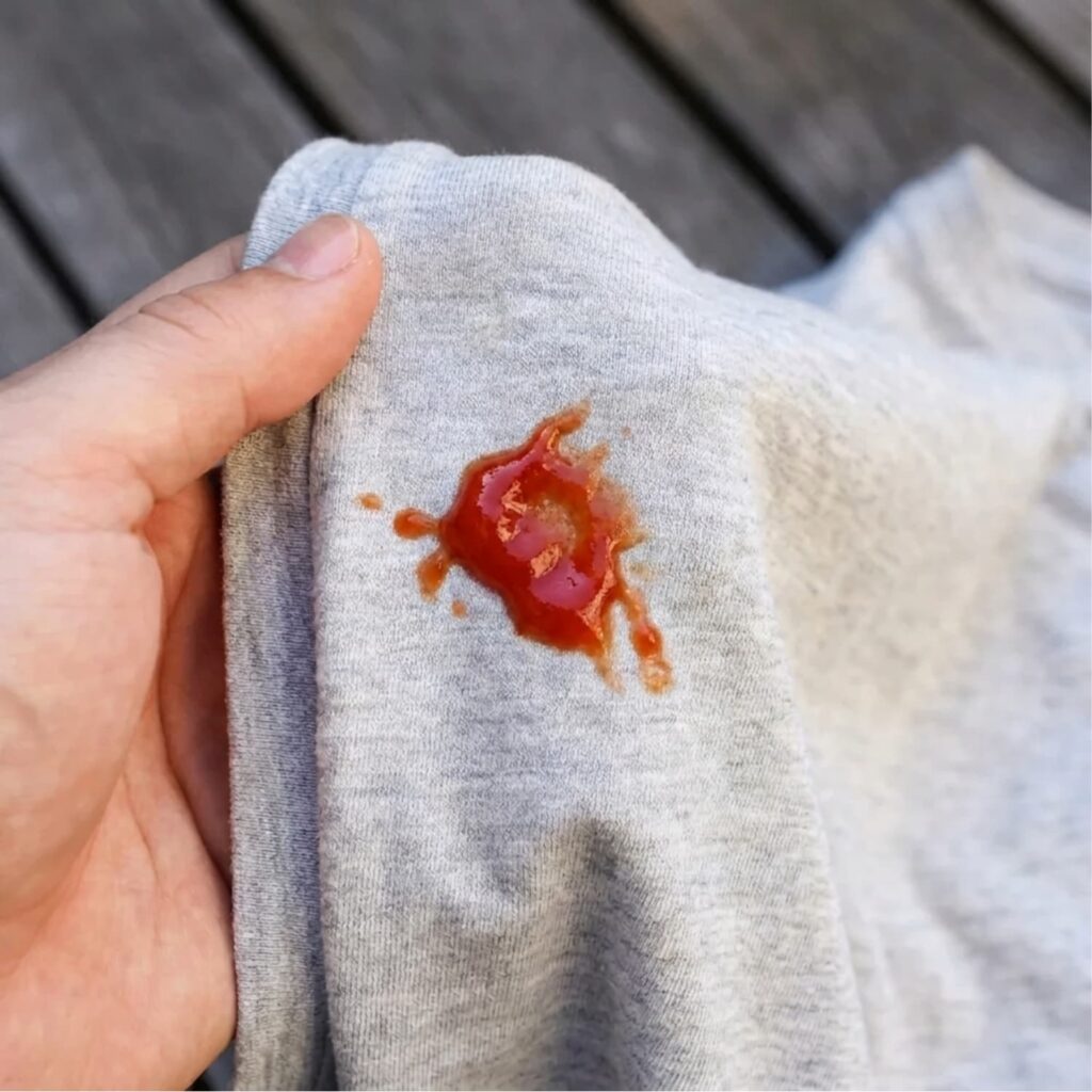 Person holding a shirt with ketchup stain.