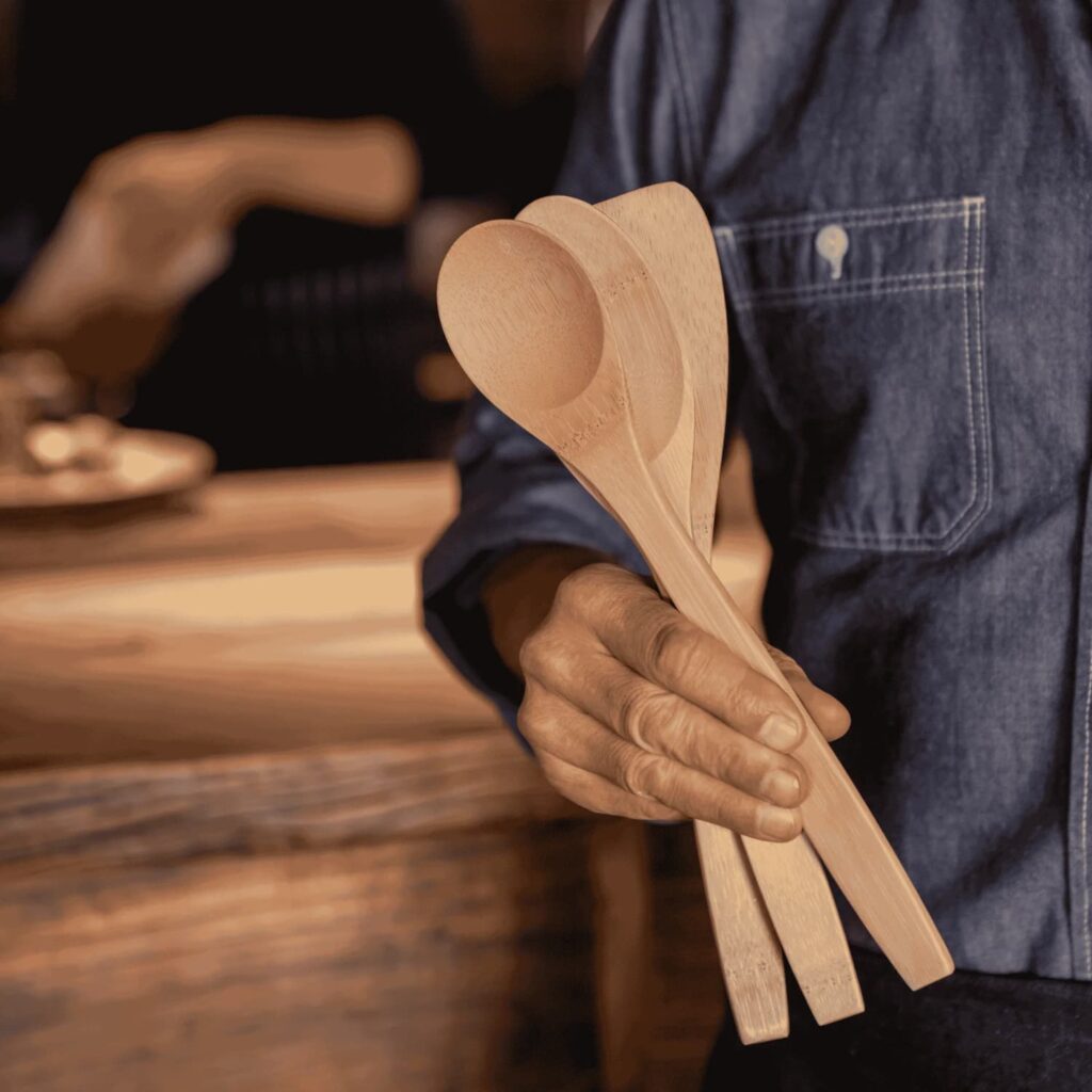 Man standing by a table holding bamboo utensils for cooking.