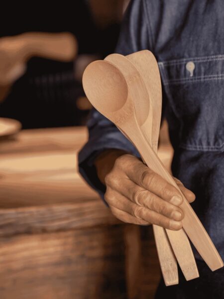 Man standing by a table holding bamboo utensils for cooking.