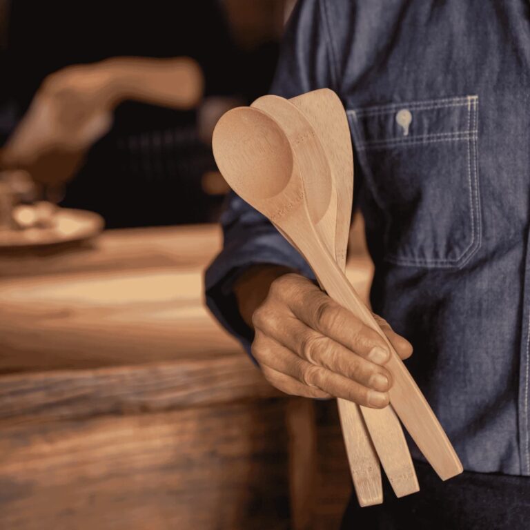 Man standing by a table holding bamboo utensils for cooking.