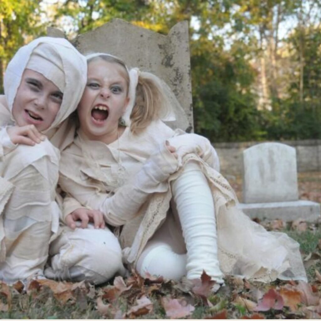 A boy and girl in DIY mummy costumes in a grave yard.