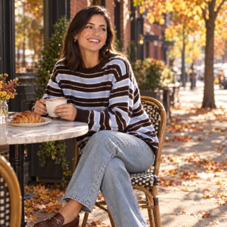 Woman in a brown and blue striped recycled cashmere sweater at a sidewalk cafe in the fall, one of the best sustainable sweaters