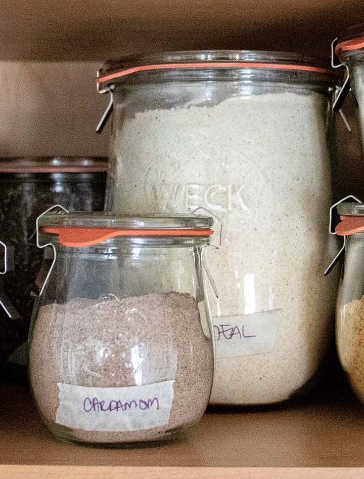 Weck glass jars with glass lids, rubber rings, and metal clamps holding spices and flour on a pantry shelf